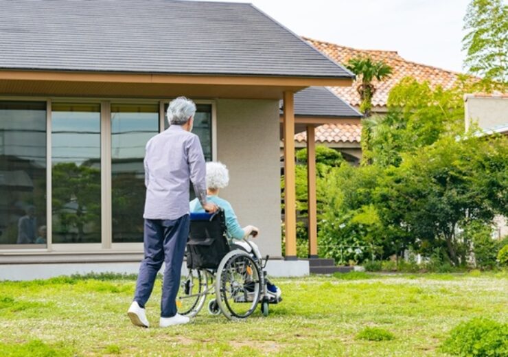 Senior,Couple,In,Wheelchairs,Walking,In,Front,Of,Their,House