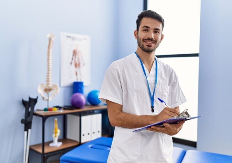 Young,Hispanic,Man,Wearing,Physiotherapist,Uniform,Writing,On,Clipboard,At